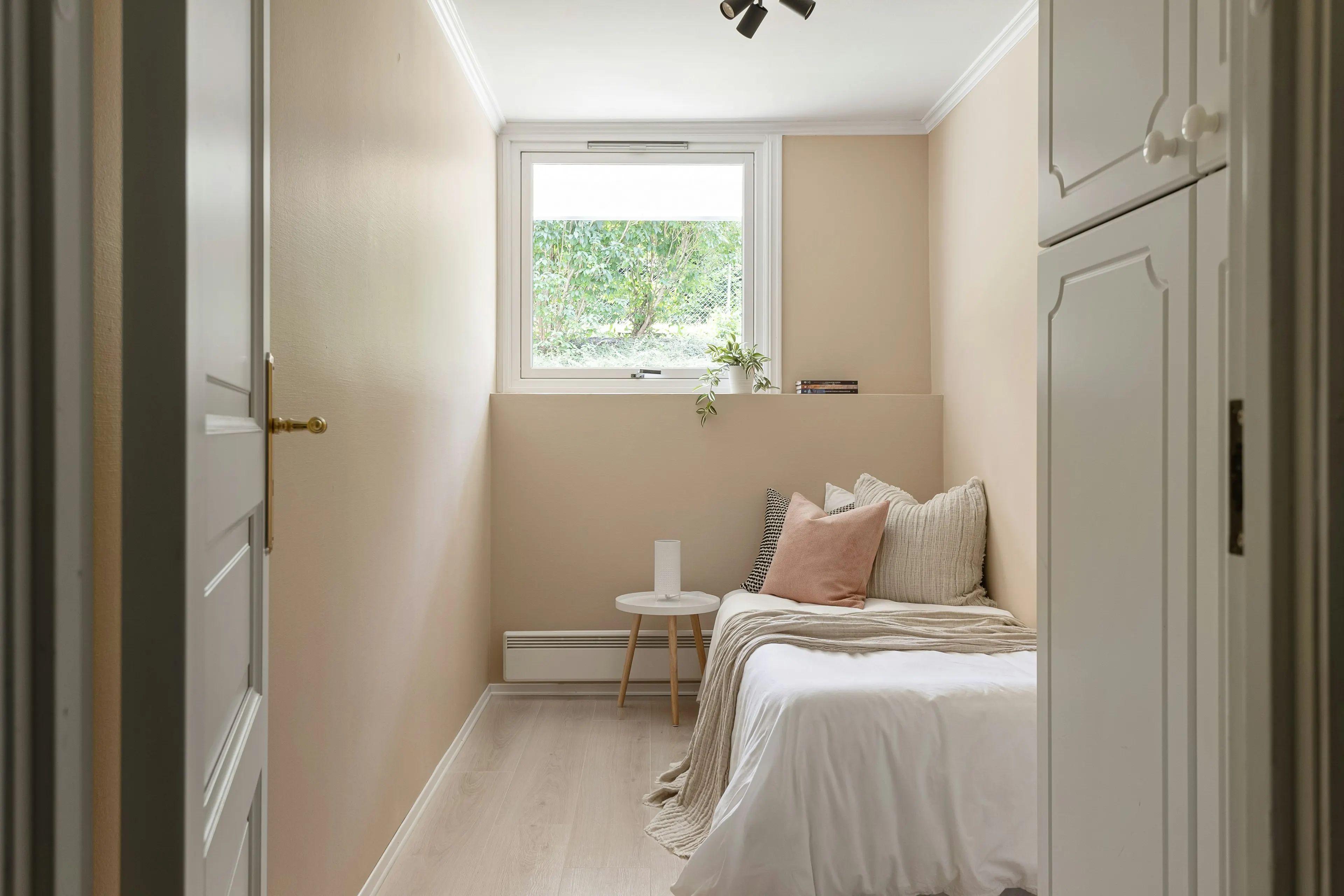 Single bed with a blush cushion by a garden window (reference image)